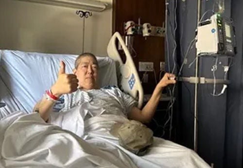 Man in hospital bed with thumbs up.