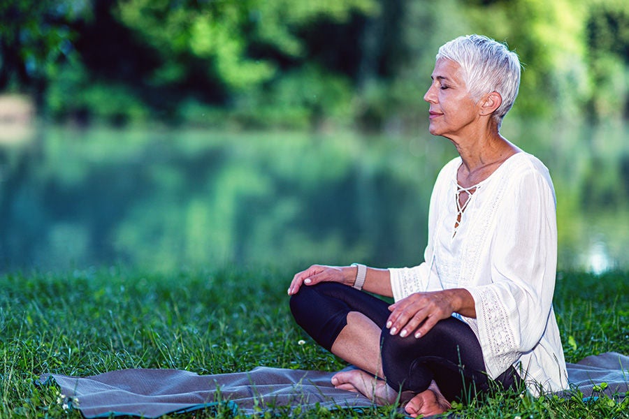 Person meditating sitting outside on the grass.