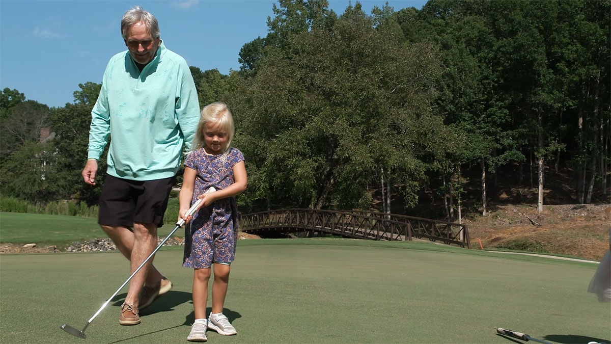 Person on golf course with child holding a golf club.