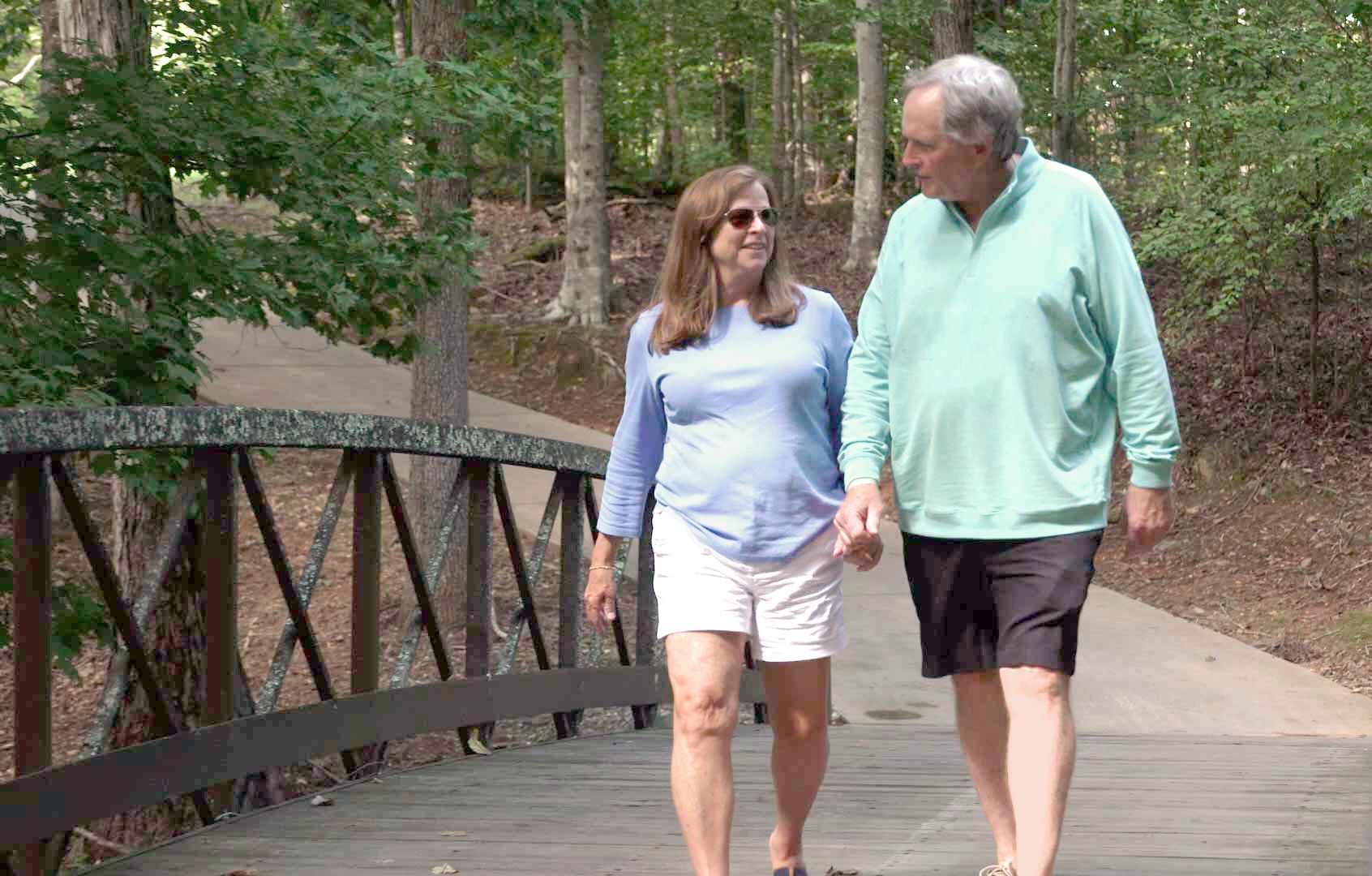 Two people holding hands while walking on a wooded pedestrian bridge