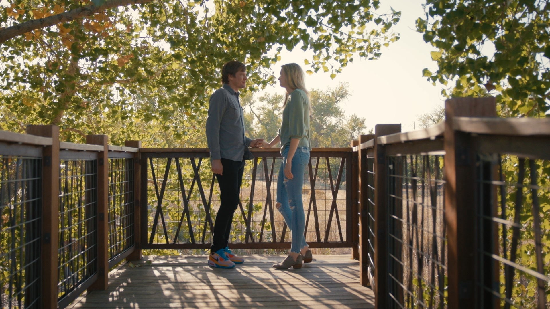 Two people standing on a bridge facing each other.