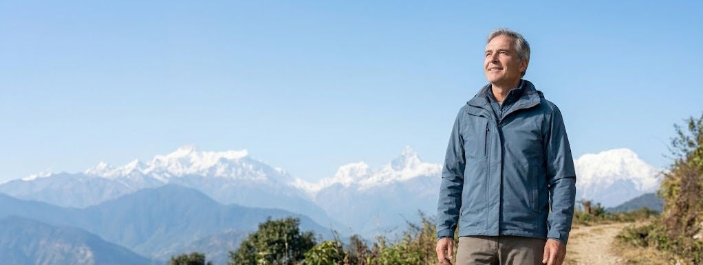 Person standing on a mountain trail with snow-covered peaks in the distance.